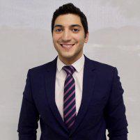 Dr. Daniel Navi, smiling, in a navy suit, white shirt and a striped purple tie